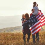 Family in field with American flag, children on shoulders.