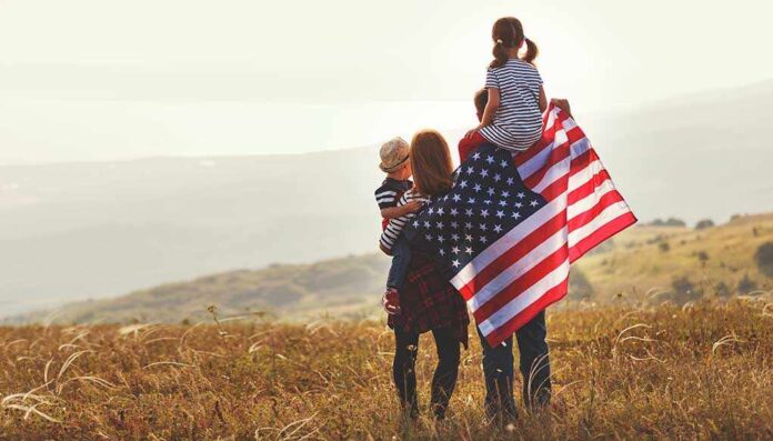 1117095815 featured image Family in field with American flag, children on shoulders.