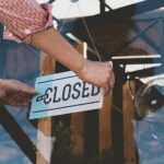 Hand placing closed sign on glass door