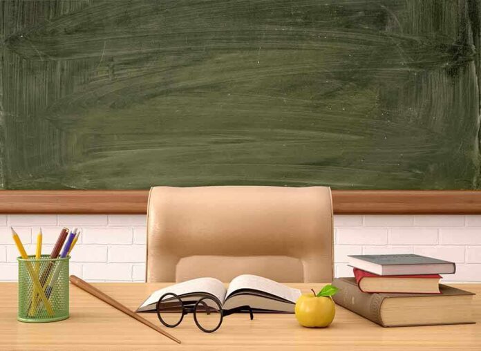 Classroom desk with books, apple, and chalkboard.