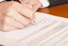 Hand signing a document on wooden desk