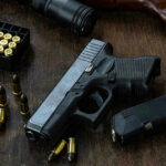 Handgun with ammunition, magazine, and rifle on wooden table