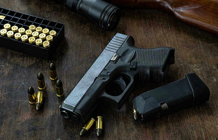 Handgun with ammunition, magazine, and rifle on wooden table