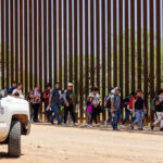 People walking beside tall fence and border patrol vehicle.
