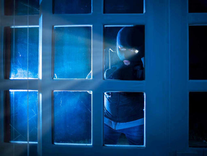 Masked figure peering through glass door at night