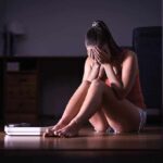 A young woman sitting on the floor with her head in her hands, looking distressed
