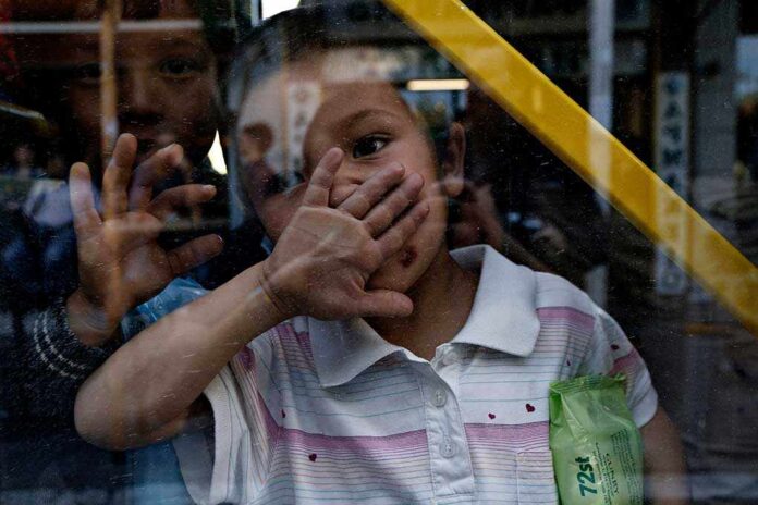 A child playfully covering their face while looking through a glass window