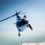 A helicopter flying over a mountainous landscape under a blue sky