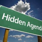 Road sign displaying the phrase Hidden Agenda against a blue sky