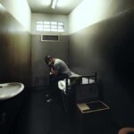 A person sitting in a dimly lit prison cell, appearing contemplative and distressed