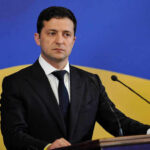 Man in suit speaking at podium with microphones.