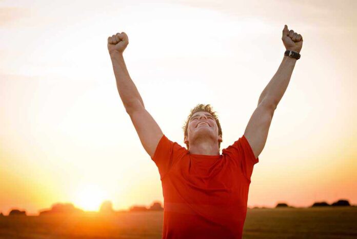 shutterstock_152853110.jpg Man in a red shirt celebrating with arms raised against a sunset
