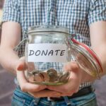 Person holding a glass jar labeled DONATE filled with coins
