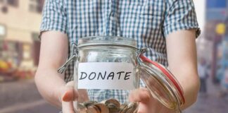 Person holding a glass jar labeled DONATE filled with coins