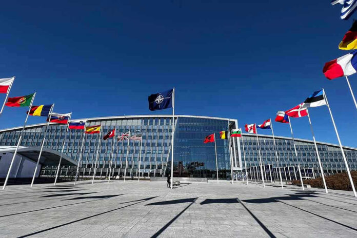 Flags outside NATO headquarters building under clear blue sky.
