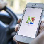 Phone Wait Times SLASHED – More Progress COMING A person holding a smartphone displaying the Google Maps app while driving