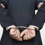 A person in a suit with hands cuffed behind their back