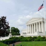 The U.S. Supreme Court building with an American flag and landscaped grounds