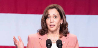 Woman speaks at podium with red and white background.