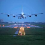 An airplane approaching the runway at night with landing lights illuminated