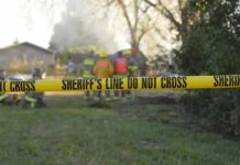Yellow police tape marking a restricted area at a fire scene with firefighters in the background