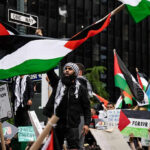 Protesters with flags and signs, one holding a megaphone.