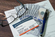 Medicare card glasses pen money on wooden table