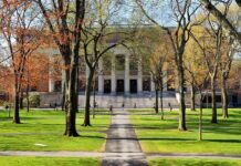 Students walking on a university campus with autumn trees and a historic building in the background
