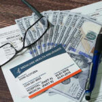 Fed Holds Rates Steady While Quietly Dropping Talk of Cuts Medicare card glasses pen money on wooden table
