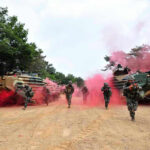 Soldiers running from armored vehicles with red smoke.