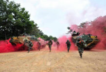 Soldiers running from armored vehicles with red smoke.