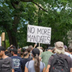 Crowd holds No More Mandates sign at protest.