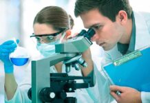 FDA Fast-Track After Kids Defy Deadly Tumor Two scientists conducting an experiment in a laboratory, one looking through a microscope and the other holding a flask with blue liquid