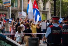 Cuba’s Cruel Twist: Freedom Equals Exile Crowd of protesters holding flags and signs behind police tape