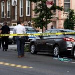Police at urban street crime scene with yellow tape around parked cars