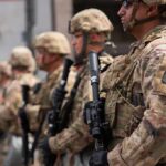 Soldiers in camouflage gear stand in formation holding rifles