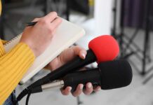 Journalist holding two microphones while writing in a notebook
