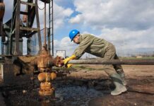 Worker in blue hard hat operating rusty oil pump equipment outdoors