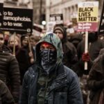 Protester wearing a bandana mask amid a crowd holding signs