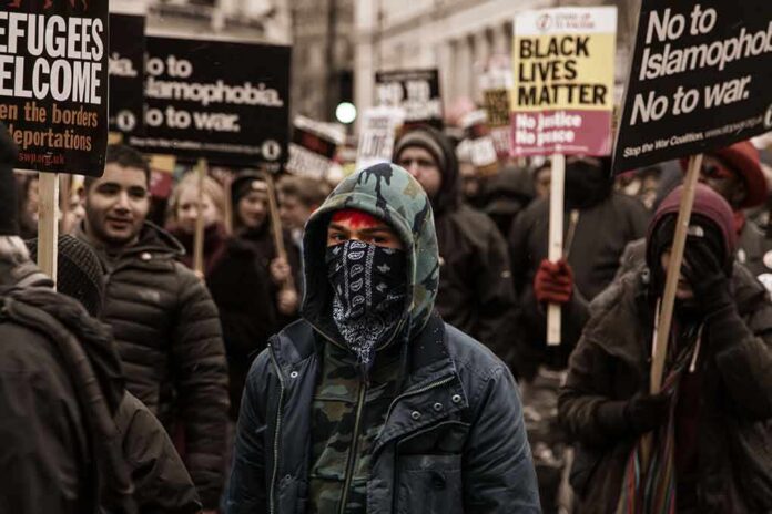 shutterstock_1230557026 Protester wearing a bandana mask amid a crowd holding signs