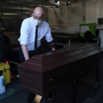 Funeral worker in mask moving a wooden coffin on a trolley