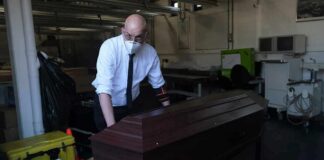 Funeral worker in mask moving a wooden coffin on a trolley