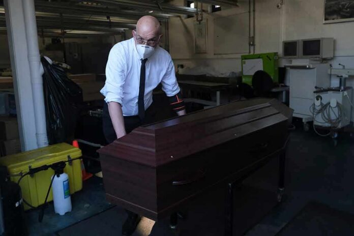 Funeral worker in mask moving a wooden coffin on a trolley