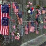 9/11 Gatekeepers Target The Mayor Memorial wall adorned with American flags and flowers