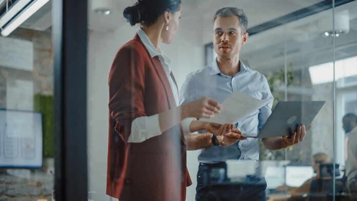 Two colleagues discussing documents in a glass-walled office