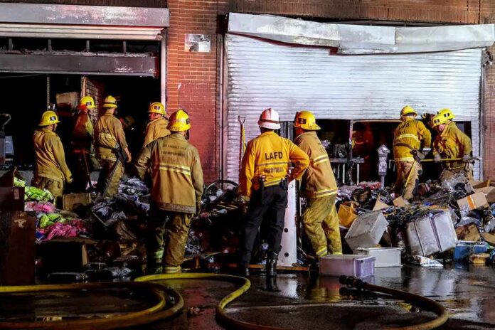 Firefighters work outside a damaged warehouse with debris and hoses