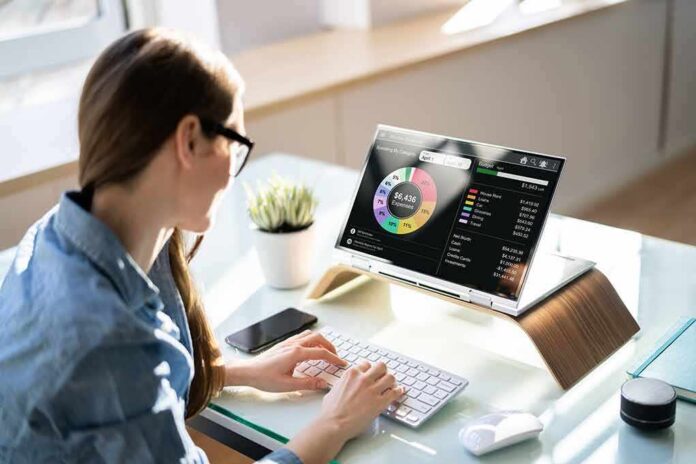 shutterstock_2136984013 Woman working at desk with laptop showing finance dashboard