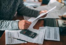 The AI Bubble Just POPPED And They’re Coming For Your 401(k) Person reviewing bills with calculator at cluttered desk