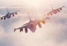 Three fighter jets flying in formation above clouds at sunrise