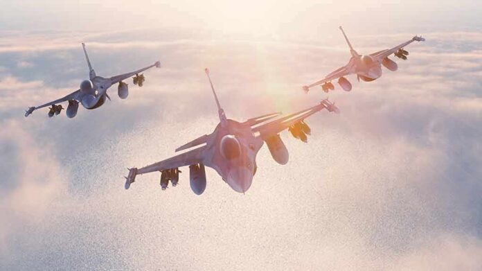 Three fighter jets flying in formation above clouds at sunrise
